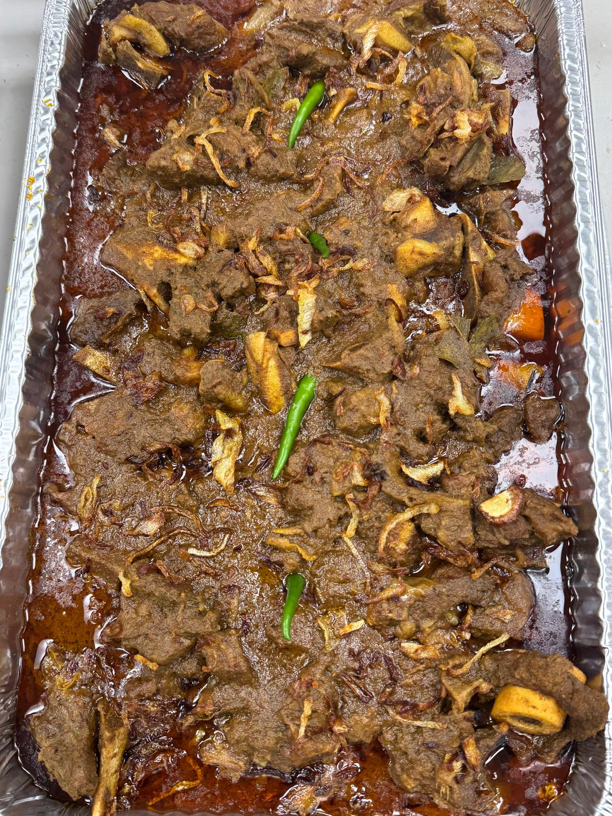 Full tray of slow-cooked beef curry with crispy fried onions and green chilies